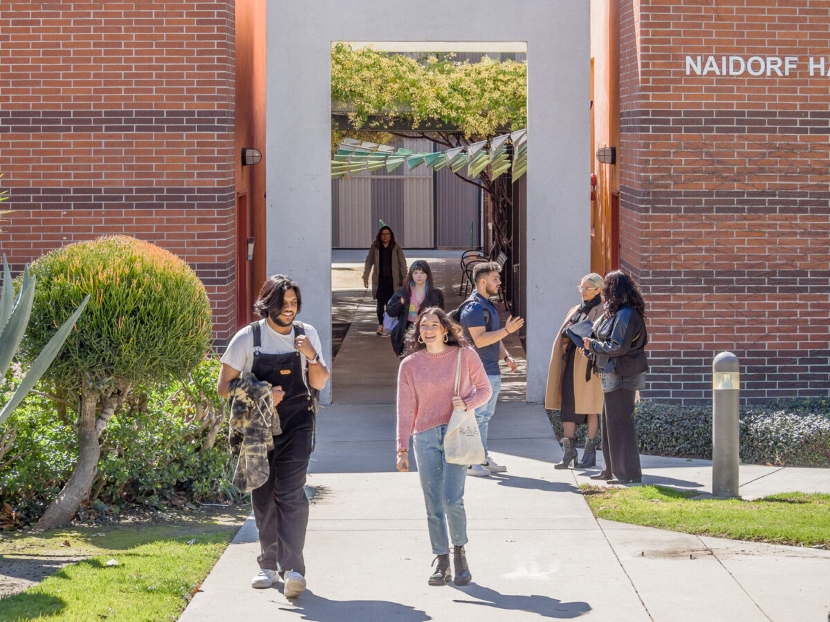 Two students walking in front of a brick building carrying bags.